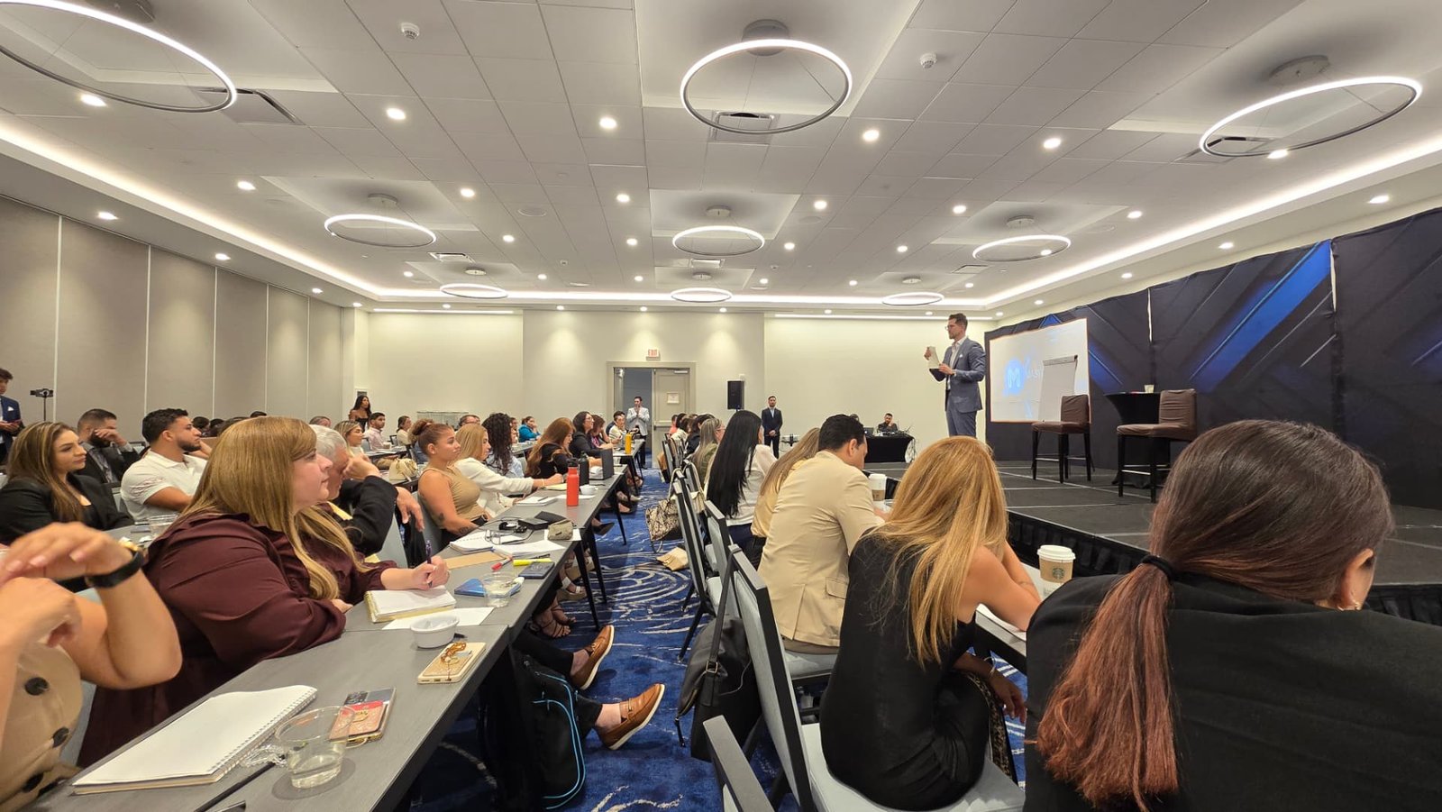 Capacitación empresarial en sala de entrenamiento con participantes tomando notas.